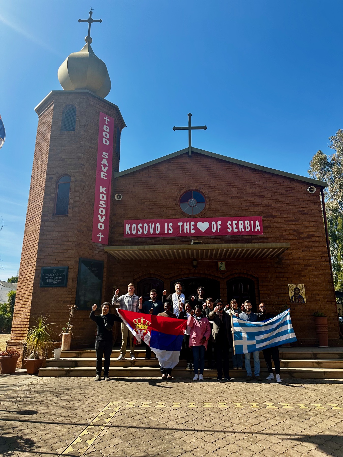 Parishioners standing proudly with Serbian and Greek flags outside the church