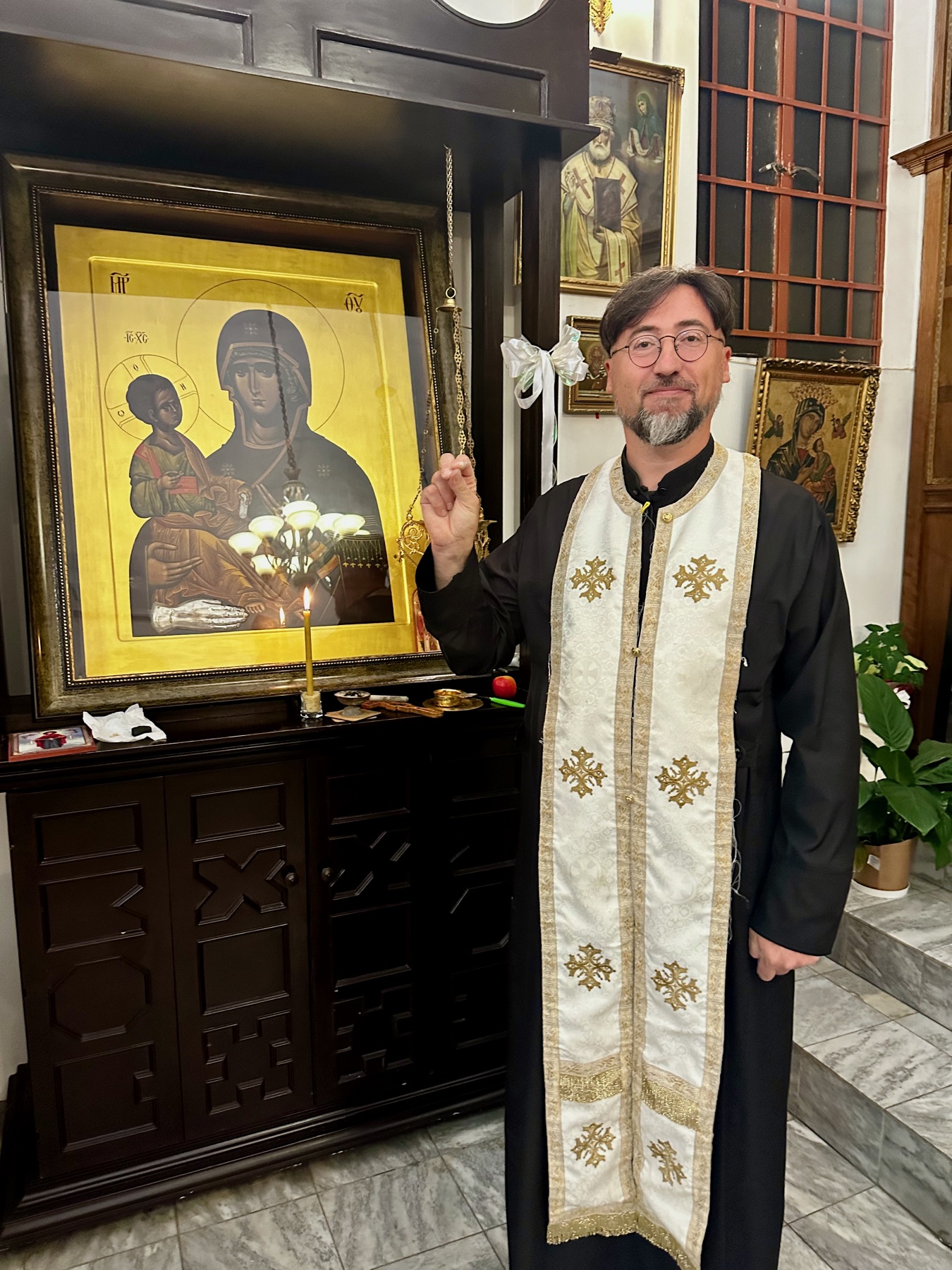 Father Isajlo standing in front of the Icon of the Three Hands